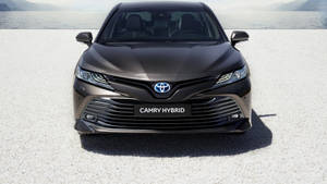 深灰色豐田Camry Hybrid的前視圖，在礫石上靠近水邊，背景有山脈。