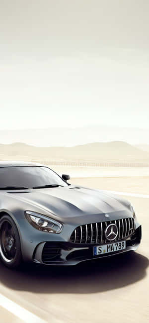 銀色 Mercedes-AMG GT 在沙漠公路上奔馳，背景有山脈。 — POCO M8s 壁紙
