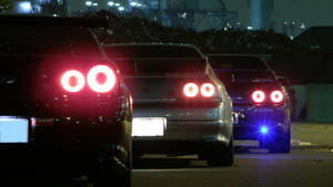 三輛帶有發光紅色尾燈的跑車夜間停放在工業區。