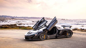 黑色McLaren跑車，車門打開，停在日落時分的海邊公路上。 — 麥拿侖 GIF 壁紙