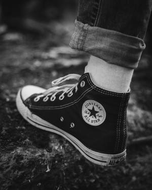 特寫一個人穿著黑色 Converse All Star 運動鞋，搭配捲起的牛仔褲。