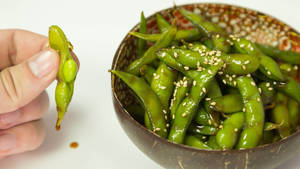 手拿毛豆莢放在芝麻毛豆碗上方。