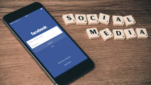 智能手機顯示Facebook登入畫面，旁邊有拼出社交媒體的Scrabble字母牌在木頭上。
