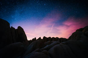 在充滿活力的星空暮色下，深色岩層呈現紫色和藍色調。