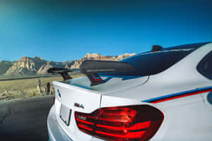 白色BMW M4性能車配備碳纖維尾翼，停在沙漠中靠近山脈，夕陽時分。