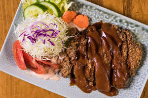 酥脆炸肉排配棕色醬汁和新鮮沙律，放在有紋理的碟子上。