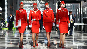 四位身穿紅色制服的女空服員在機場客運大樓內行走。