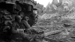 兩名士兵在毀壞的城市區域中於戰車旁休息。