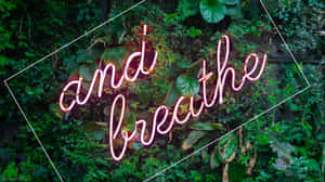 粉紅色霓虹燈牌寫著「and breathe」，被綠色樹葉包圍。