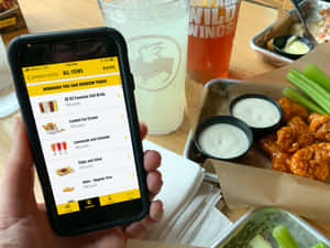 在Wild Wings餐廳用手機兌換獎勵，桌上放有雞翼和飲料。