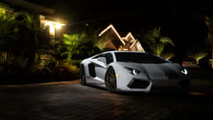白色林寶堅尼Aventador夜間在房屋燈光下停泊，伴有棕櫚樹。