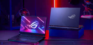 兩部 ROG 遊戲筆記型電腦，帶有發光螢幕和 RGB 燈光，放在遊戲桌上。