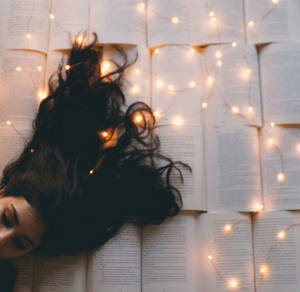 深色頭髮的人躺在打開的書上，周圍有發光的串燈。