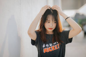 穿著米奇老鼠T恤的年輕女性在白色牆壁附近觸碰頭髮。