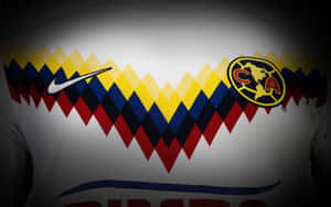 白色足球球衣特寫，帶有紅、黃、藍色鋸齒圖案和 Club America 徽章。
