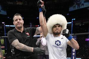 戴白色帽子的UFC拳手在八角籠中慶祝勝利，裁判舉起他的手。