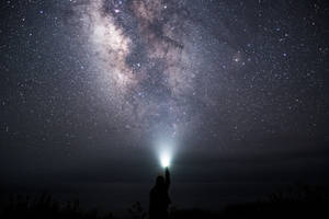 人將手電筒指向天空，顯現銀河星辰