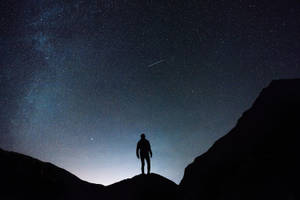 站在山頂上，下方是星空，有銀河和流星。