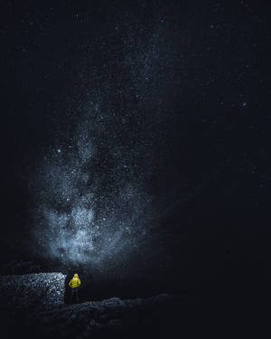 穿著黃色外套的人站在岩石上，星空下
