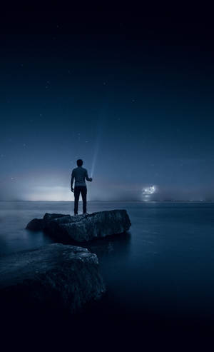 夜晚站在岩石上的人將手電筒照向水面上方的星空