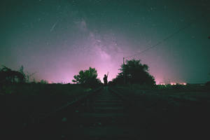 一個人的剪影站在火車軌道上，背景是星光燦爛的紫色夜空。