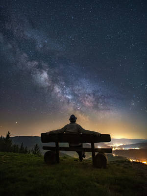 人坐在長椅上，星空下俯瞰山谷燈光