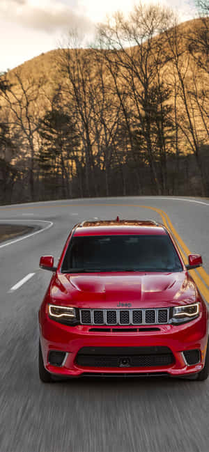 紅色Jeep SUV在日落時分行駛在蜿蜒的山路上。