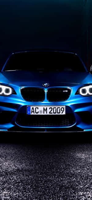 藍色BMW M2跑車在夜間於黑暗瀝青上被照亮。 — Galaxy A54 壁紙