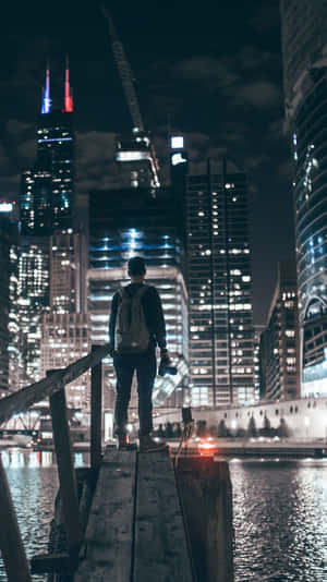 夜晚站在碼頭上眺望燈火通明的城市天際線的人。