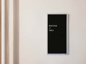 一個黑色邊框的勵志語錄標牌，上面寫著「WHATEVER IT TAKES」，位於白色牆上。