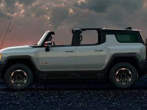 暮色中碎石上的銀色電動Hummer EV，伴隨著色彩繽紛的雲彩。