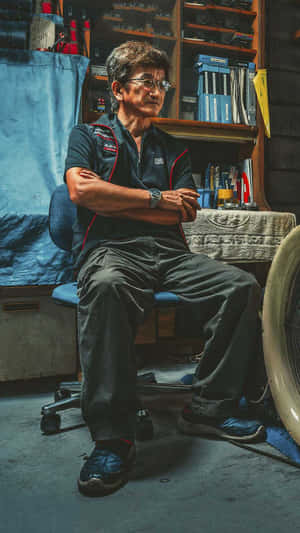 一位嚴肅的男子穿著賽車制服坐在雜亂的車庫中。 — 肖像 壁紙