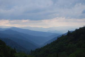 陰雲密布的暮色天空下，層層疊疊的山峰和森林構成的寧靜山景。