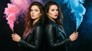 兩個穿著皮褸的女人在黑暗背景下手持粉紅色和藍色煙霧信號彈。