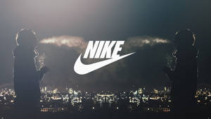 兩個人影映襯在明亮的城市天際線前，中央有一個大型Nike標誌。 — 吸煙 壁紙