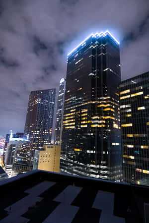從屋頂觀看的夜景，城市天際線中燈火通明的摩天大樓和多雲的天空。