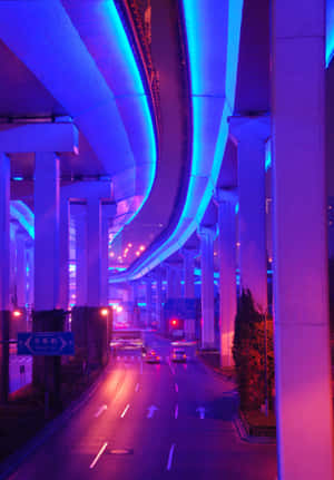 夜晚霓虹燈照亮的高速公路，汽車在發光的藍色和粉紅色結構下行駛。 — 霓虹藍色美學 壁紙