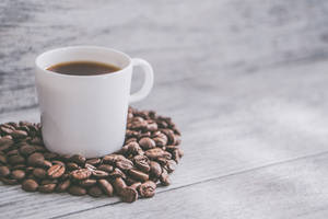 白色咖啡杯被咖啡豆包圍，放在木桌上
