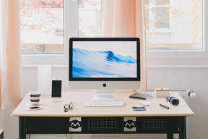 簡約家居辦公桌，配有iMac、電話、眼鏡和杯子，在柔和窗光下。