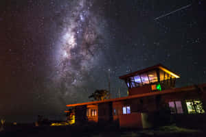 一座現代建築在夜晚星空下被照亮，銀河清晰可見。 — 月色夜空 壁紙