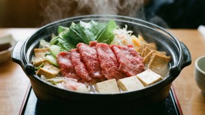 冒著熱氣的鍋，有牛肉、豆腐和蔬菜，在木桌上