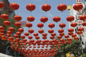 一排排紅色燈籠懸掛在節日氣氛的都市街景上方。 — 中國新年 壁紙