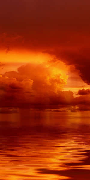 平靜水面上充滿活力的橙色和紅色夕陽，伴隨著發光的雲朵。 — 橙色美學 壁紙