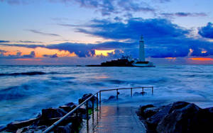 黃昏時分岩石島上的燈塔，伴隨著戲劇性的雲彩和海浪。