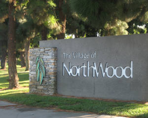 一個為 The Village of NorthWood 而設的石製標誌，位於長滿青草、有松樹的公園內。