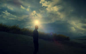 一個男人獨自站在沙丘上，看著太陽在黃昏時分穿過烏雲。