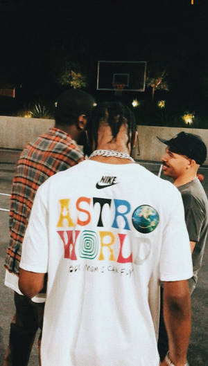 三個男人夜晚喺籃球場上，其中一個着住彩色Astro World T恤。