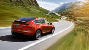 紅色Tesla Model X在蜿蜒的山路上飛馳，背景是翠綠的山丘和夕陽餘暉。 — Tesla GIF 壁紙