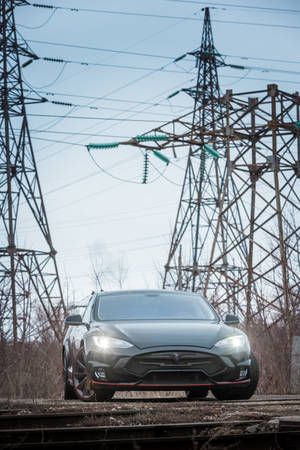 黑色Tesla Model S停泊在廢棄火車軌上，附近有電塔。