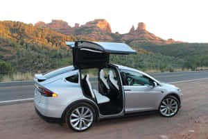 銀色 Tesla Model X 打開車門，停在日落時分紅色岩層附近的沙漠公路上。